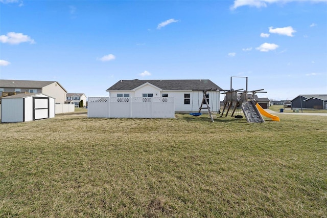 back of house with an outbuilding, fence, a storage shed, a playground, and a lawn