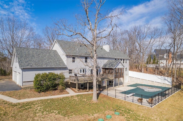 back of house with fence, a wooden deck, roof with shingles, a lawn, and a chimney