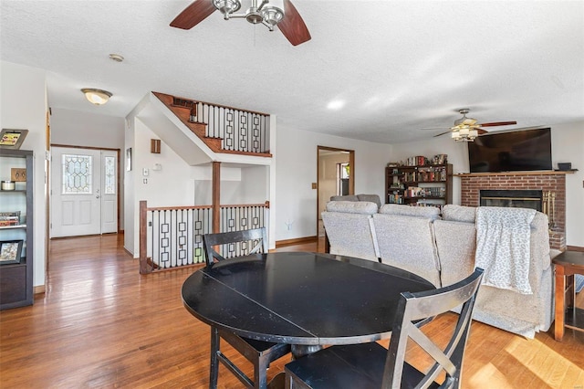 dining area featuring ceiling fan, a textured ceiling, wood finished floors, and a fireplace