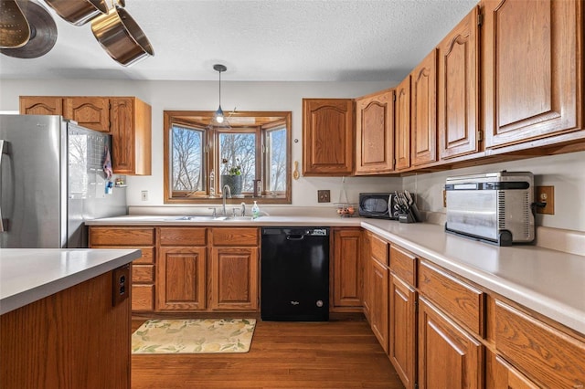 kitchen featuring black dishwasher, dark wood-style flooring, freestanding refrigerator, and brown cabinets