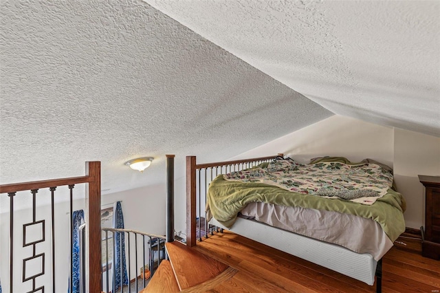 bedroom featuring lofted ceiling, a textured ceiling, and wood finished floors