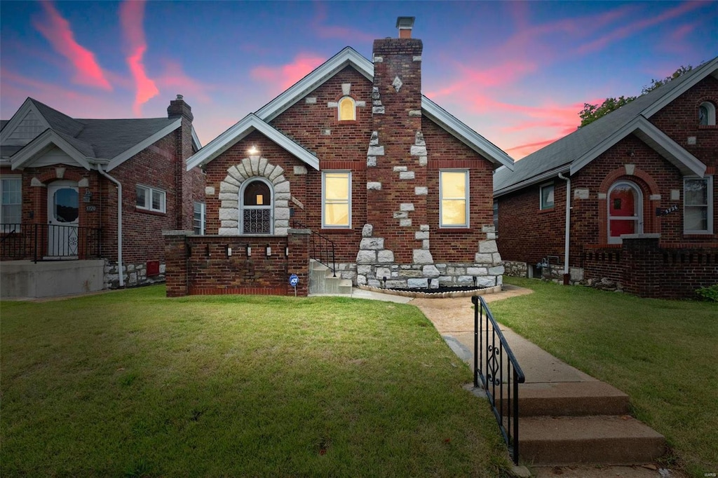 tudor-style house with a lawn, brick siding, and a chimney