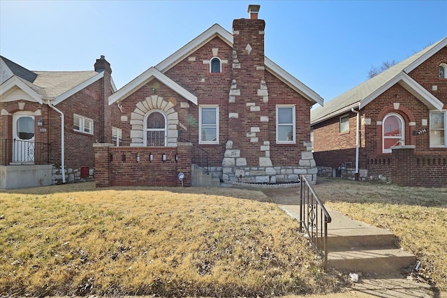 tudor-style house with a front lawn, brick siding, and a chimney