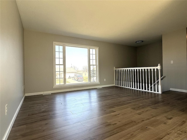 empty room featuring visible vents, baseboards, and dark wood-style flooring