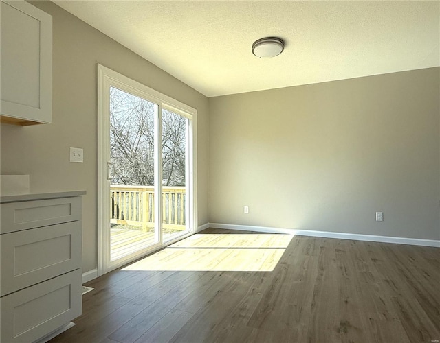 unfurnished dining area with a textured ceiling, baseboards, and dark wood-style flooring