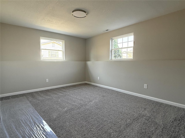 spare room with visible vents, a textured ceiling, a healthy amount of sunlight, and dark carpet