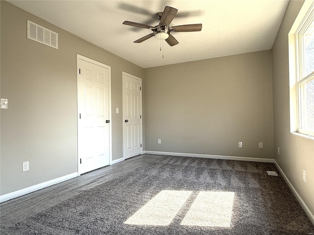 unfurnished bedroom featuring dark colored carpet, visible vents, baseboards, and a ceiling fan