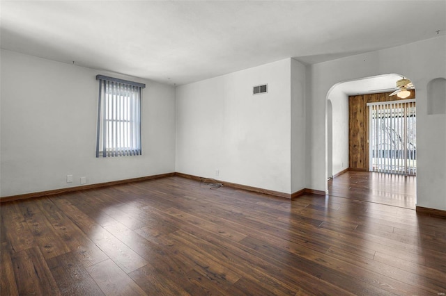 empty room with visible vents, ceiling fan, baseboards, arched walkways, and wood-type flooring