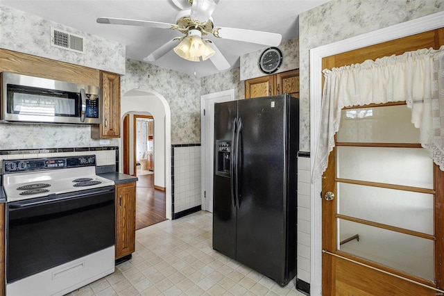 kitchen with visible vents, wallpapered walls, range with electric cooktop, stainless steel microwave, and black fridge