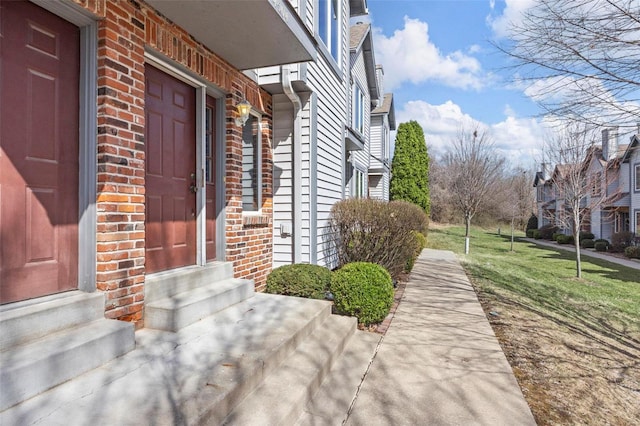 view of exterior entry featuring brick siding and a yard