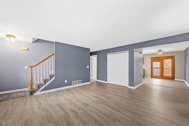 unfurnished living room with stairway, wood finished floors, visible vents, and baseboards