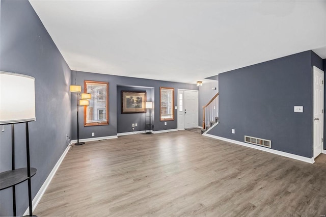 unfurnished living room with stairs, wood finished floors, visible vents, and baseboards