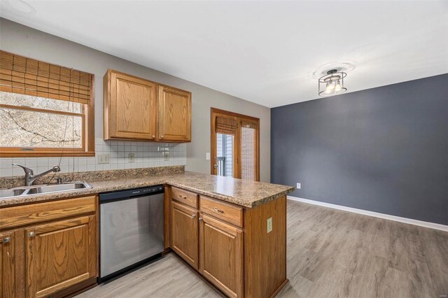 kitchen with light wood finished floors, a peninsula, a sink, dishwasher, and backsplash