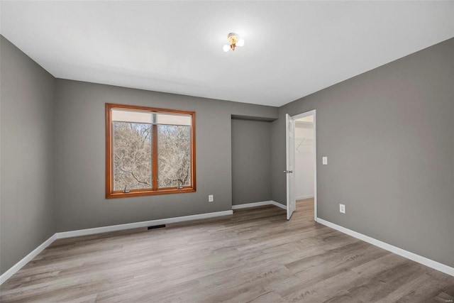 unfurnished bedroom featuring light wood-type flooring, baseboards, visible vents, and a closet