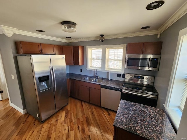 kitchen featuring a sink, dark stone countertops, appliances with stainless steel finishes, crown molding, and light wood finished floors