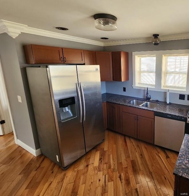 kitchen with light wood-style flooring, ornamental molding, appliances with stainless steel finishes, and a sink