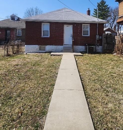 view of front of home featuring brick siding, a chimney, a front yard, and fence