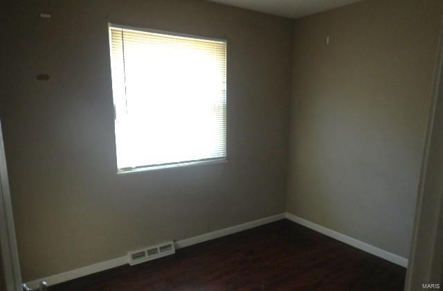 empty room featuring visible vents, baseboards, and dark wood-type flooring