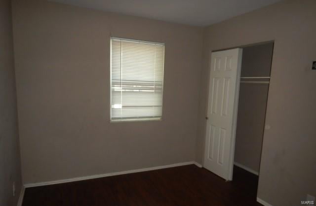 unfurnished bedroom featuring dark wood finished floors, baseboards, and a closet