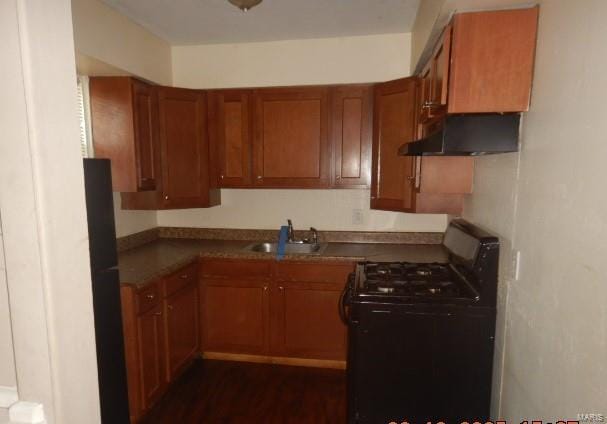 kitchen with a sink, dark wood-type flooring, black range with gas cooktop, under cabinet range hood, and brown cabinets