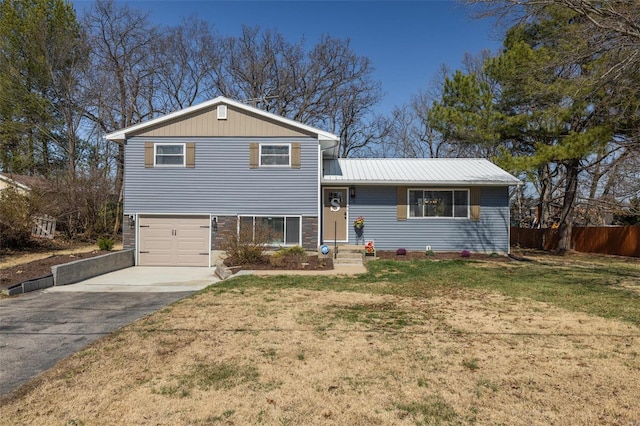 tri-level home with a front yard, fence, driveway, an attached garage, and metal roof