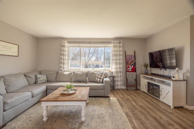 living room featuring a glass covered fireplace, baseboards, and wood finished floors