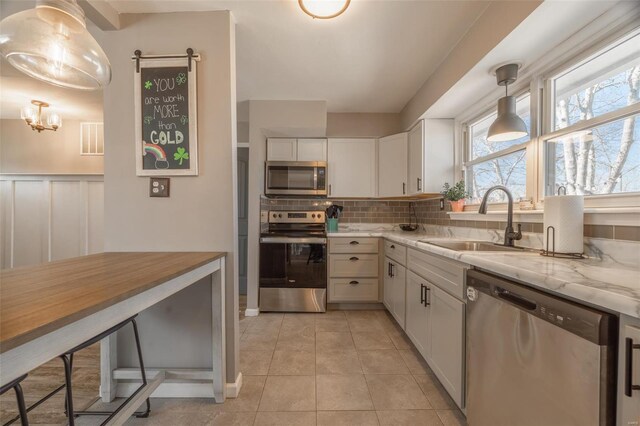 kitchen featuring a sink, backsplash, white cabinetry, stainless steel appliances, and light tile patterned floors