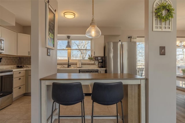 kitchen with backsplash, a kitchen bar, light countertops, stainless steel appliances, and a sink