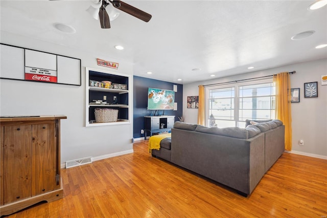 living room featuring visible vents, built in shelves, baseboards, and wood finished floors