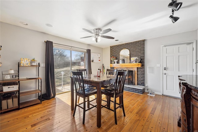 dining area with baseboards, a ceiling fan, light wood-style flooring, and a fireplace