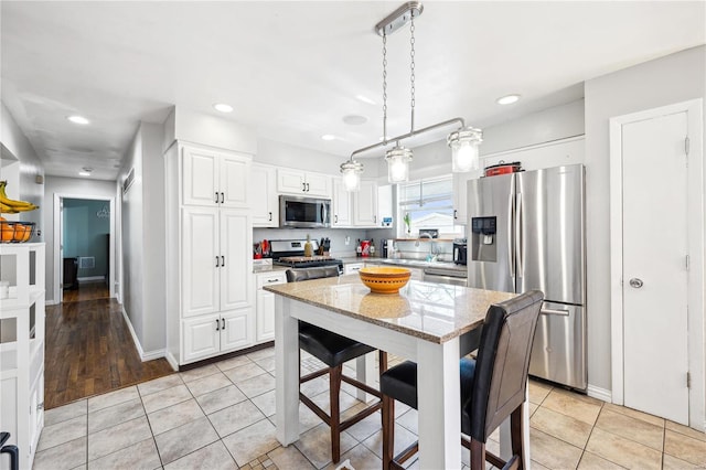 kitchen with light stone countertops, light tile patterned floors, hanging light fixtures, white cabinets, and stainless steel appliances