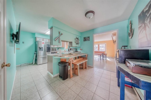 kitchen featuring baseboards, a peninsula, light tile patterned flooring, stainless steel fridge with ice dispenser, and light countertops