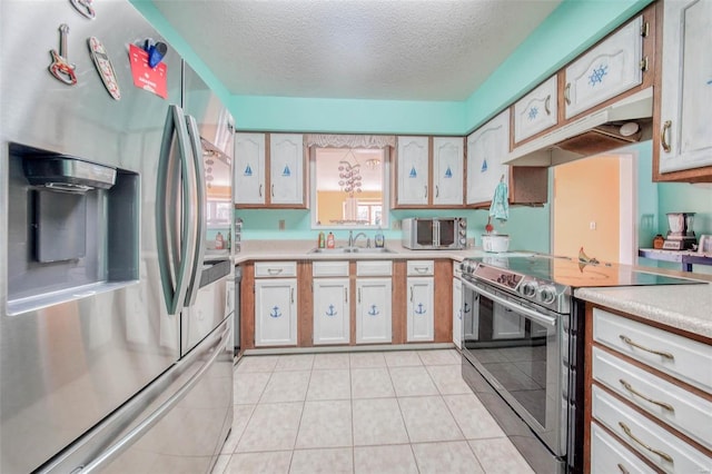 kitchen with light countertops, light tile patterned floors, stainless steel appliances, a textured ceiling, and a sink