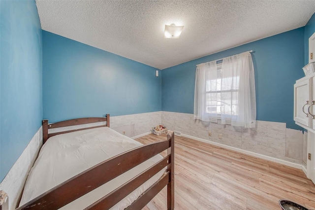 bedroom featuring a wainscoted wall, a textured ceiling, and wood finished floors