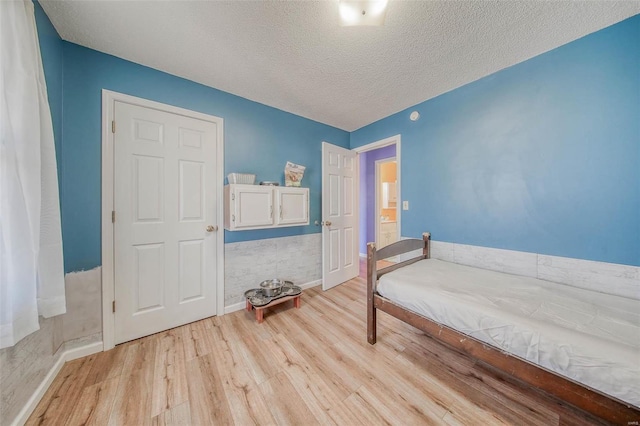 bedroom featuring light wood finished floors, a textured ceiling, and baseboards