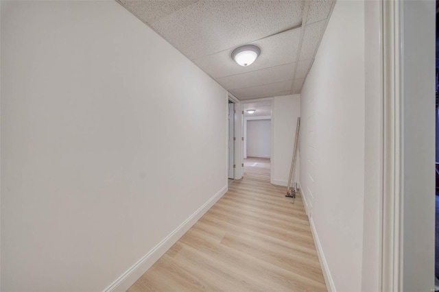 corridor with a paneled ceiling, light wood-type flooring, and baseboards