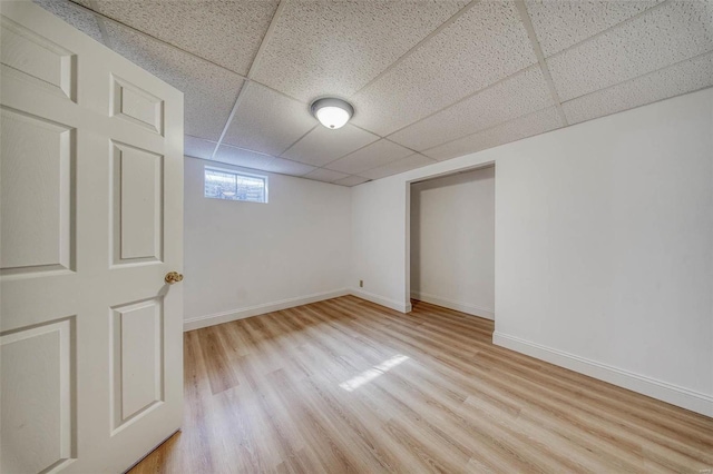 basement featuring a paneled ceiling, baseboards, and light wood-style floors