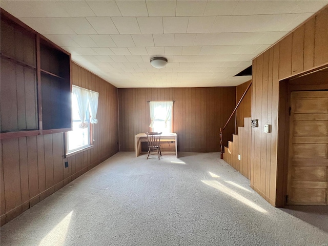 empty room featuring stairway, light carpet, and wood walls