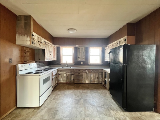 kitchen with electric range, wood walls, freestanding refrigerator, and a sink