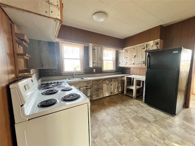 kitchen featuring a sink, white range with electric stovetop, freestanding refrigerator, wood walls, and light countertops