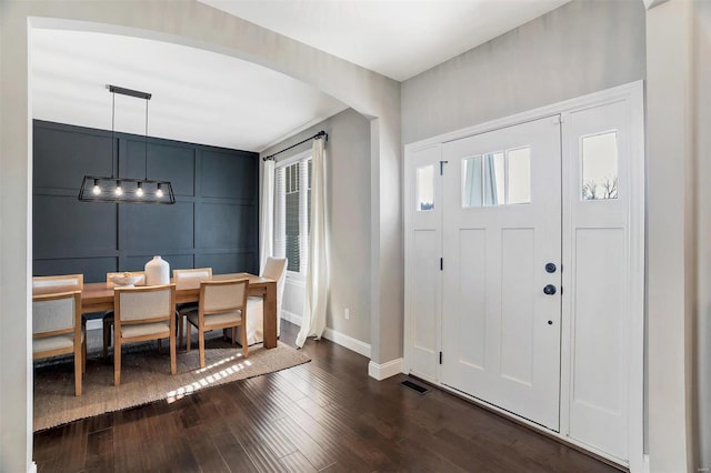 foyer entrance featuring visible vents, baseboards, arched walkways, a decorative wall, and dark wood-style flooring