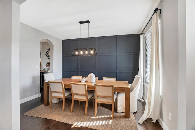 dining room with a decorative wall, dark wood-style floors, arched walkways, and baseboards