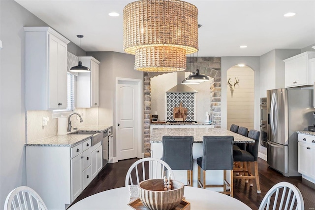 kitchen with a sink, a kitchen island, stainless steel appliances, white cabinetry, and dark wood-style flooring