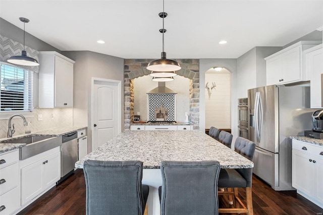 kitchen with a breakfast bar area, dark wood-style flooring, a sink, appliances with stainless steel finishes, and backsplash