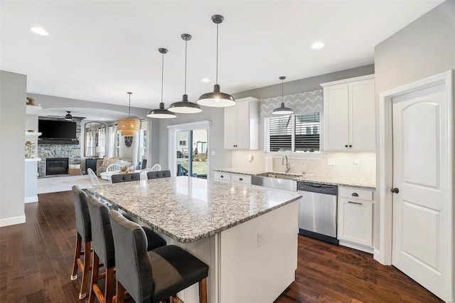 kitchen with a sink, backsplash, stainless steel dishwasher, a center island, and a fireplace