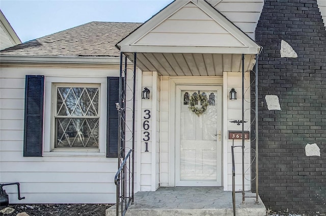 view of exterior entry with roof with shingles