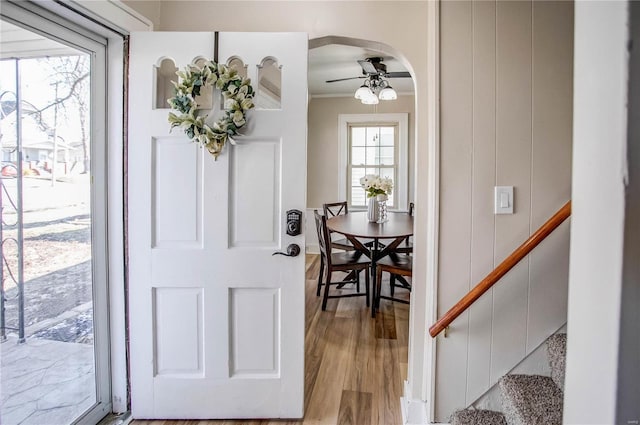 foyer entrance featuring a ceiling fan, light wood finished floors, arched walkways, ornamental molding, and stairs