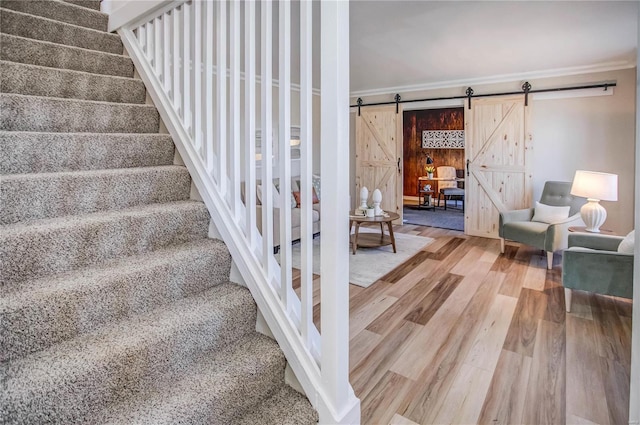 stairway featuring ornamental molding, a barn door, and wood finished floors