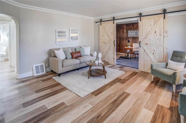 living room featuring visible vents, light wood finished floors, arched walkways, ornamental molding, and a barn door