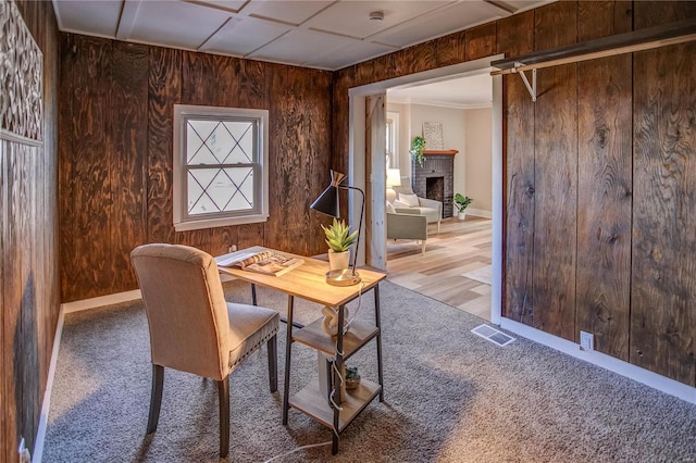 home office featuring a brick fireplace, wooden walls, visible vents, and carpet floors